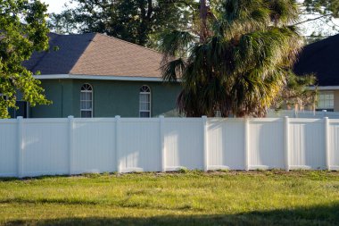 Bahçeyi çevreleyen yeşil çimlerde bahçe koruması ve mahremiyet için beyaz vinil çitler..