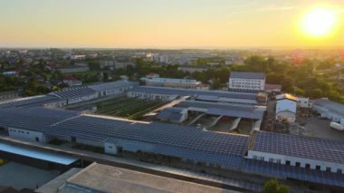 Günbatımında yeşil ekolojik elektrik üretmek için endüstriyel bina çatısına monte edilen mavi fotovoltaik güneş panellerinin hava görüntüsü. Sürdürülebilir enerji konsepti üretimi.