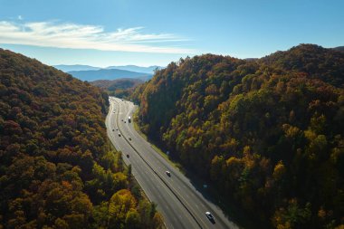 Aerial view of I-40 freeway in North Carolina leading to Asheville through Appalachian mountains in golden fall with fast moving trucks and cars. Interstate transportation concept.