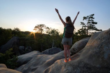 Young woman hiker standing alone with outstretched arms on mountain footpath enjoying view of evening nature on wilderness trail. Active way of life concept.