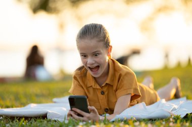 Mutlu kız çocuğu yaz parkında cep telefonuyla sosyal medyada geziniyor..