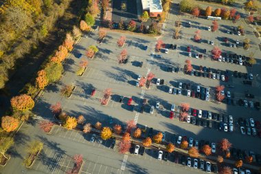 Aerial view of large parking lot with many parked colorful cars. Carpark at supercenter shopping mall with lines and markings for vehicle places and directions.