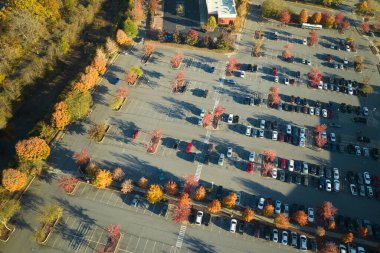 Aerial view of large parking lot with many parked colorful cars. Carpark at supercenter shopping mall with lines and markings for vehicle places and directions. clipart