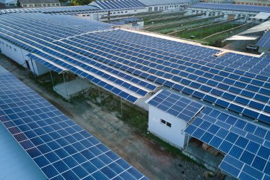 Sanayi binasının çatısına yeşil ekolojik elektrik üretmek için monte edilmiş mavi fotovoltaik panelli güneş enerjisi santralinin hava görüntüsü. Sürdürülebilir enerji konsepti üretimi.