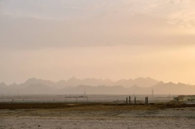 Sunset landscape with dark mountain peaks in egyptian desert and high voltage power lines.