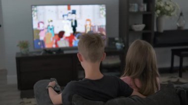 Evde televizyon izleyen erkek ve kız kardeşlerin dikiz görüntüsü. Çocuklar kanepede oturup çizgi film izliyorlar.