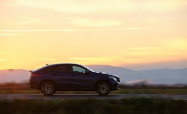 Gün batımında şehirlerarası yolda hızla giden bir SUV arabası. Akşamları otoyol trafiği.