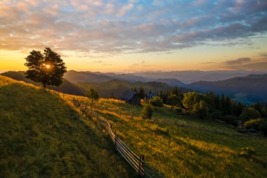 Yamaçtaki eski köylü evi. İnanılmaz bir dağ manzarası. Vahşi Ulusal Park Dağları 'nda parlak renkli gün batımı. Sarı batan güneşle aydınlatılmış koyu ladin ormanları..