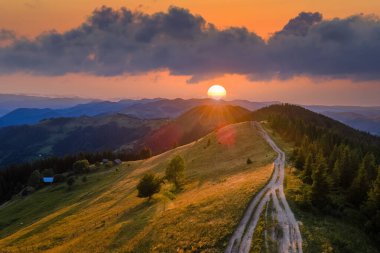 İnanılmaz bir dağ manzarası. Vahşi Ulusal Park Dağları 'nda parlak renkli gün batımı. Tepenin tepesinde kıvrılan karanlık toprak yol sarı batan güneşle aydınlanıyor..