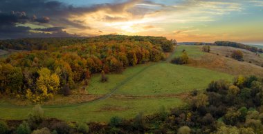 Sonbahar mevsiminde gün batımında, renkli, yemyeşil ormanlar boyunca off-road patikası. Sonbahar ormanlarındaki ağaç gölgelikleri. Sonbahar vahşi doğasının manzarası.