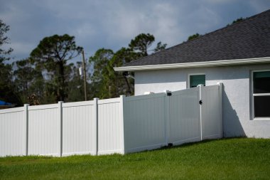 Bahçeyi çevreleyen yeşil çimlerde bahçe koruması ve mahremiyet için beyaz vinil çitler..