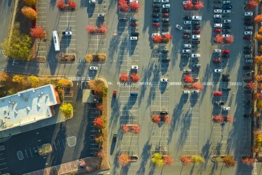 Aerial view of large parking lot with many parked colorful cars. Carpark at supercenter shopping mall with lines and markings for vehicle places and directions.