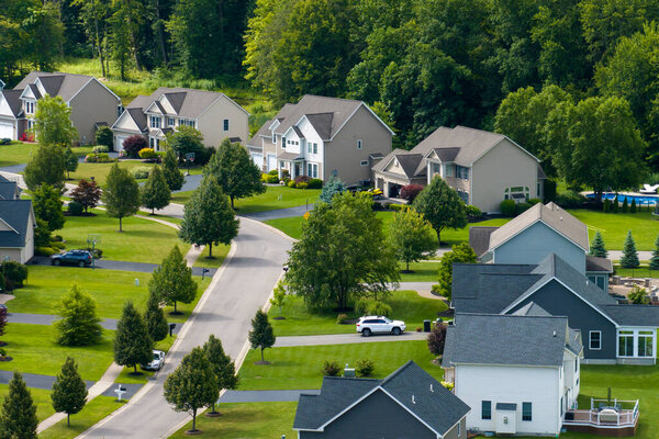 Aerial view of private residential houses in rural suburban sprawl area in Rochester, New York. Upscale suburban homes with large backyards and green grassy lawns in summer season.