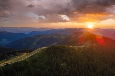 Parlak batan güneşle aydınlanan karanlık çam ormanı. Vahşi dağlarda renkli günbatımının havadan görünüşü. Güzel doğa manzarası.