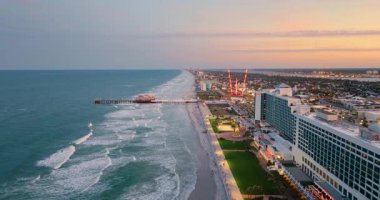 Gün batımında Daytona Plajı 'nda. Okyanus kıyısındaki eğlence parkının önündeki ana cadde iskelesi ve aydınlatılmış otel ve apartman daireleri. Florida, ABD 'deki turizm altyapısı