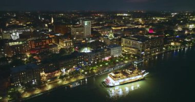 Savannah, Georgia 'da. Eski tarihi River Caddesi ve nehir teknesi su üzerinde ilerliyor. Gece aydınlık sokakların yukarıdan görünüşü. ABD turizm merkezi