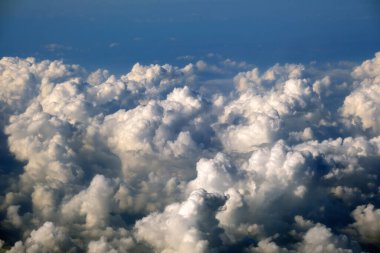 Yüksek irtifada, yoğun kümülüs bulutlarının uçtuğu uçak penceresinden hava görüntüsü.
