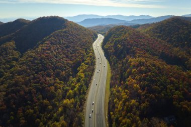 Aerial view of I-40 freeway in North Carolina leading to Asheville through Appalachian mountains in golden fall with fast moving trucks and cars. Interstate transportation concept.