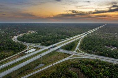 Florida 'da otoyol kavşağında gün batımında Amerikan kırsal kesiminde hızlı giden trafik arabaları ve kamyonlar var. ABD 'de eyaletler arası ulaşım altyapısı.