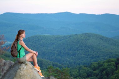 Sportif kadın yamaç yolunda tek başına oturuyor. Kadın yürüyüşçü vahşi yoldaki kayalık kayalıklardan doğanın tadını çıkarıyor. Etkin yaşam tarzı kavramı.