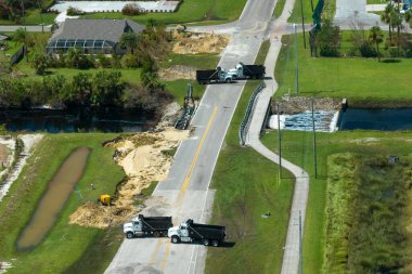 Yol çalışması alanındaki inşaat kamyonları. Sel suları asfaltı yıktıktan sonra nehir tarafından yıkılan hasarlı yol köprüsünün yeniden inşasındaki barikat. Yıkılmış ulaşım altyapısının yeniden inşası.