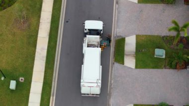 Çöp kamyonu Amerikan mahallesinin kaldırımından çöp kutusu yüklüyor.