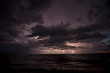 Akşamları gök gürültüsü ve gök gürültüsü ile fırtınalı kara bulutlar kumlu kumsala vuran deniz dalgaları. Gün batımında deniz manzarası.