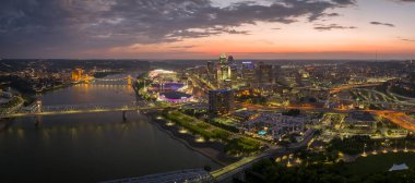 Cincinnati city, Ohio, USA with bridge highway traffic driving cars in downtown district. American city skyline with brightly illuminated high commercial buildings at night.