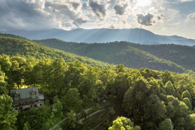Tepedeki ev ve Kuzey Carolina Appalachian dağlarındaki Mitchell Dağı. Parlak batan güneşle aydınlanan yemyeşil orman. Vahşi dağlarda renkli günbatımının havadan görünüşü. Güzel doğa manzarası.