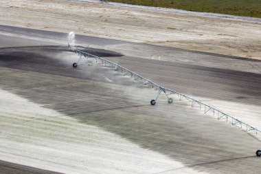 Aerial view of irrigation system watering farm field during dry season. Industrial sprinkler spraying water on farmland ground for crops growth during period of drought.