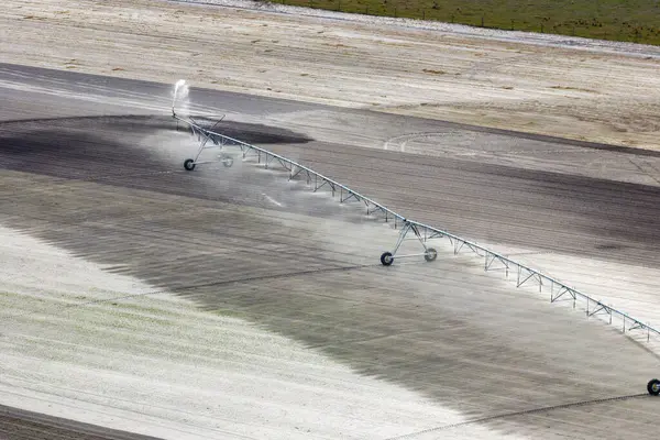 Aerial view of irrigation system watering farm field during dry season. Industrial sprinkler spraying water on farmland ground for crops growth during period of drought.