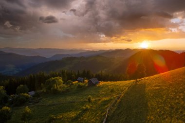 Yürüyüşçüler dağ yamacına sığınıyor. Güzel doğa manzarası. Vahşi dağlarda renkli günbatımının havadan görünüşü. Parlak batan güneşle aydınlatılmış karanlık çam ormanı..