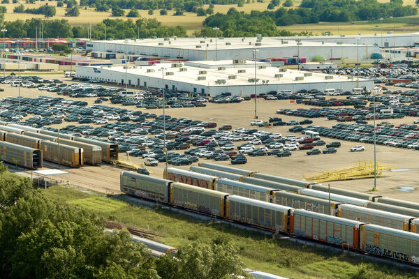 New cars loading on cargo train hauler for worldwide export on automotive factory parking lot. Dealer vehicle inventory business commercial.