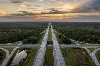 Florida 'da otoyol kavşağında gün batımında Amerikan kırsal kesiminde hızlı giden trafik arabaları ve kamyonlar var. ABD 'de eyaletler arası ulaşım altyapısı.