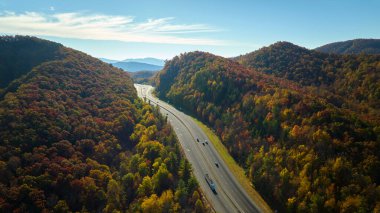 I-40 freeway road leading to Asheville in North Carolina thru Appalachian mountains with yellow fall forest and fast moving trucks and cars. Concept of high speed interstate transportation.