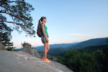 Young woman hiker standing alone on mountain footpath enjoying view of evening nature on wilderness trail. Active way of life concept.