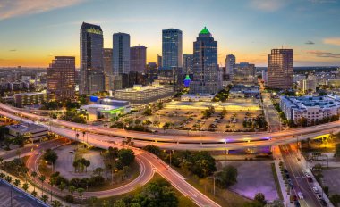 Tampa, Florida. Geniş otoyolda araba trafiği ve şehir merkezindeki yüksek gökdelenli binalar. Akşamları finans bölgesi olan Amerikan şehri
