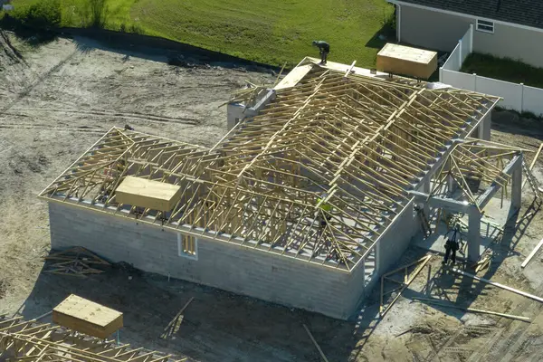 Florida 'nın banliyö bölgesinde inşaat halindeki ahşap çatı iskeleti yapısı olan bitmemiş bir ev üzerinde çalışan inşaatçıların hava görüntüsü..