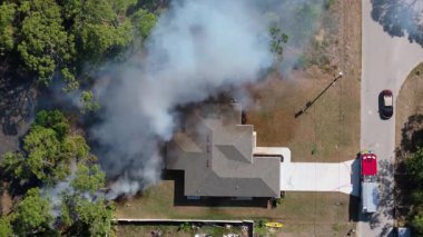 Florida 'daki banliyö evlerinin yakınlarındaki bir bitki örtüsü yangınından duman yükseliyor. İtfaiyeciler yangın bölgesini hortumla ve itfaiye araçlarıyla kapatıyor..