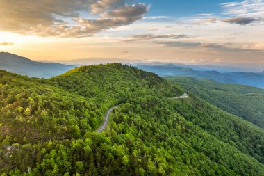 Gün batımında yaz ormanlarında dolambaçlı dağ yolu. Kuzey Carolina 'daki Appalachian dağlarında yaz mevsiminde taze yeşil orman ağaçları var. ABD doğasının güzelliği.