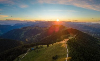 Tepenin tepesinde dönen toprak yol parlak batan güneşle aydınlanıyor. Vahşi dağlarda renkli günbatımının havadan görünüşü. Güzel doğa manzarası.