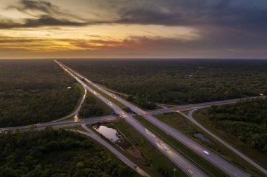 Florida 'da otoyol kavşağında gün batımında Amerikan kırsal kesiminde hızlı giden trafik arabaları ve kamyonlar var. ABD 'de eyaletler arası ulaşım altyapısı.