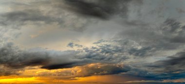 Parlak turuncu ve sarı bulutların ardında batan güneşle birlikte renkli günbatımı gökyüzü.