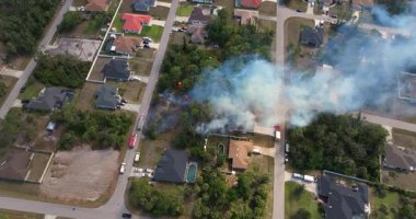 Florida 'daki banliyö evlerinin yakınlarındaki bir bitki örtüsü yangınından duman yükseliyor. İtfaiyeciler yangın bölgesini hortumla ve itfaiye araçlarıyla kapatıyor..