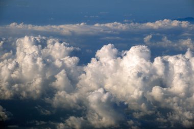 Yüksek irtifada, yoğun kümülüs bulutlarının uçtuğu uçak penceresinden hava görüntüsü.