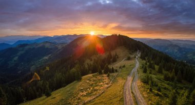 Offroad yolu tepenin üstünden geçiyor. Parlak batan güneşle aydınlanan karanlık toprak yol. Vahşi dağ ormanlarında gün batımı manzarası inanılmazdır. Güzel doğa manzarası.