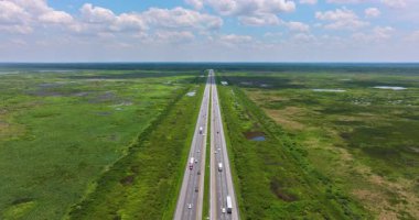 Güneşli bir günde hareket halindeki araçlarla bataklık ve sulak alanlarla çevrili Florida kırsalının hava manzarası.