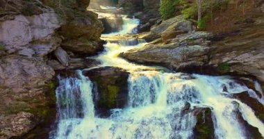 Appalachian Dağları 'ndaki Cullasaja Şelaleleri sonbahar renkleriyle çevrilidir. Orman yamaçları ve kayalık kayalar çağlayan şelaleyi çerçeveliyor.