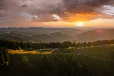 Offroad yolu tepenin üstünden geçiyor. Parlak batan güneşle aydınlanan karanlık toprak yol. Vahşi dağ ormanlarında gün batımı manzarası inanılmazdır. Güzel doğa manzarası.