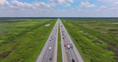 Florida otoyolunun hava manzarası mavi gökyüzünün altında hareket eden araçlarla doğal sulak araziyi kesiyor.